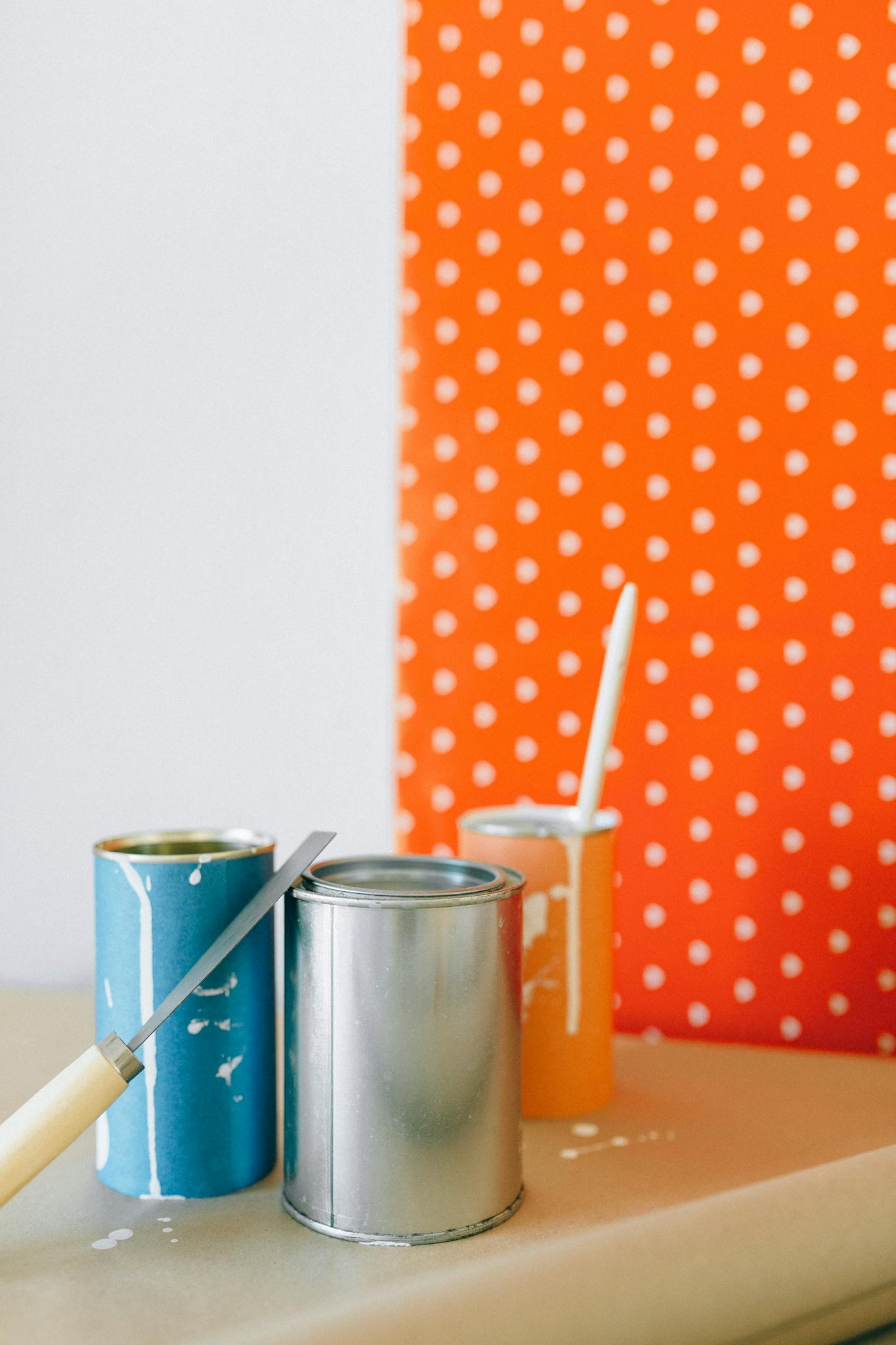 Colorful paint cans against a polka dot wallpaper ready for a home renovation.