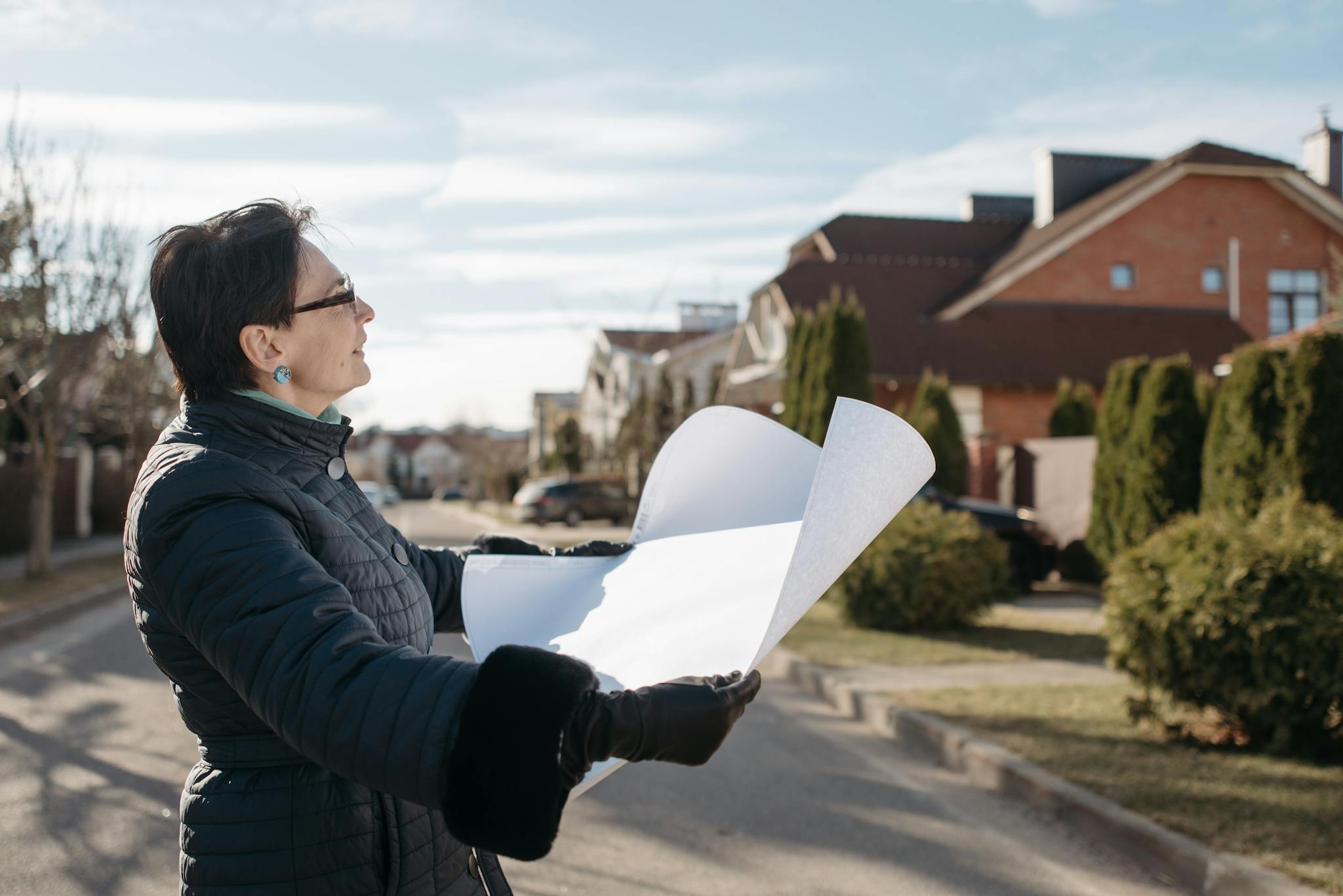 Woman in a blue jacket reviewing architectural plans outdoors on a sunny day.
